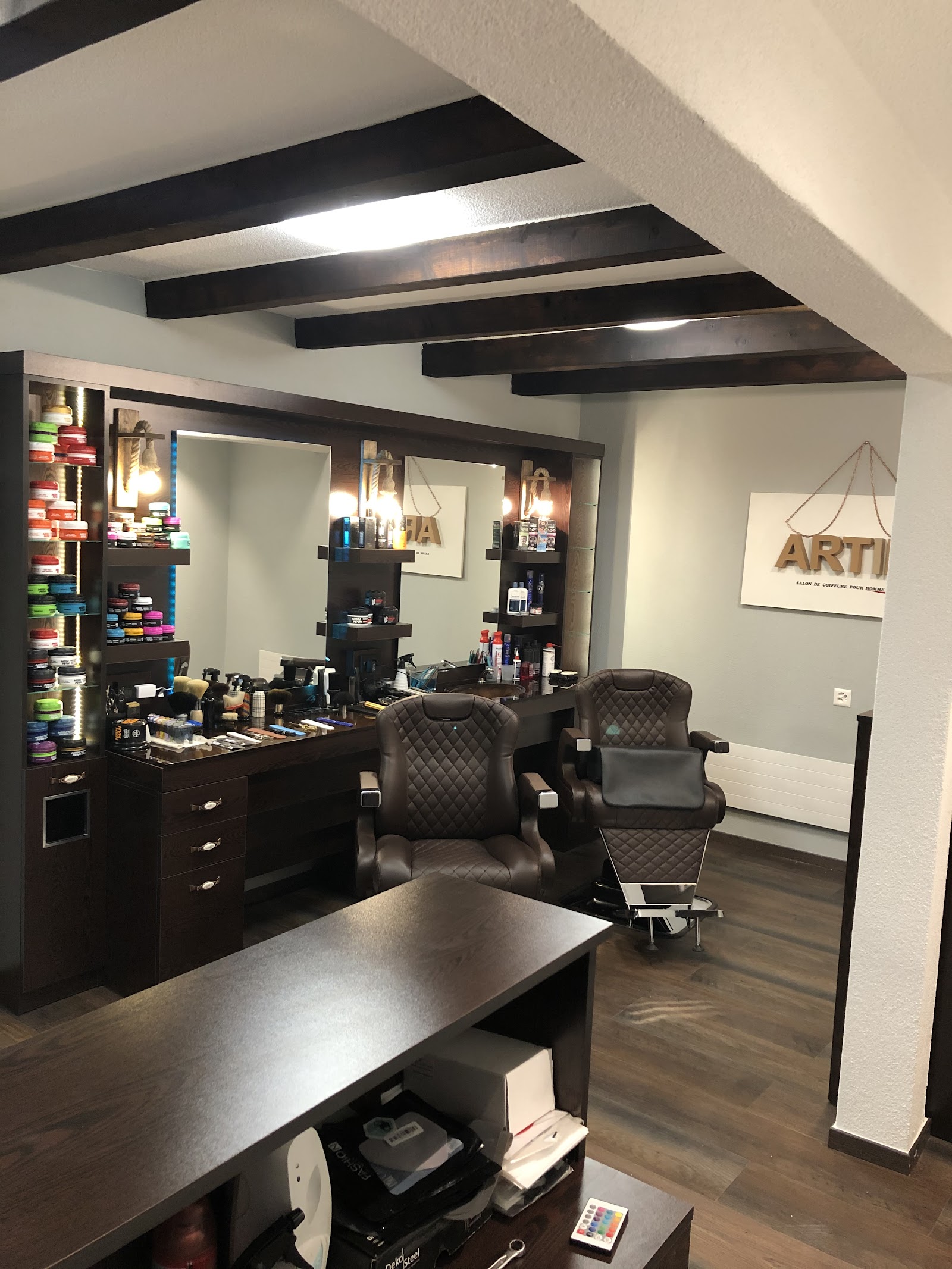Poste de travail du salon Artini — fauteuil de barbier, miroirs, produits de coiffure colorés et poutres apparentes