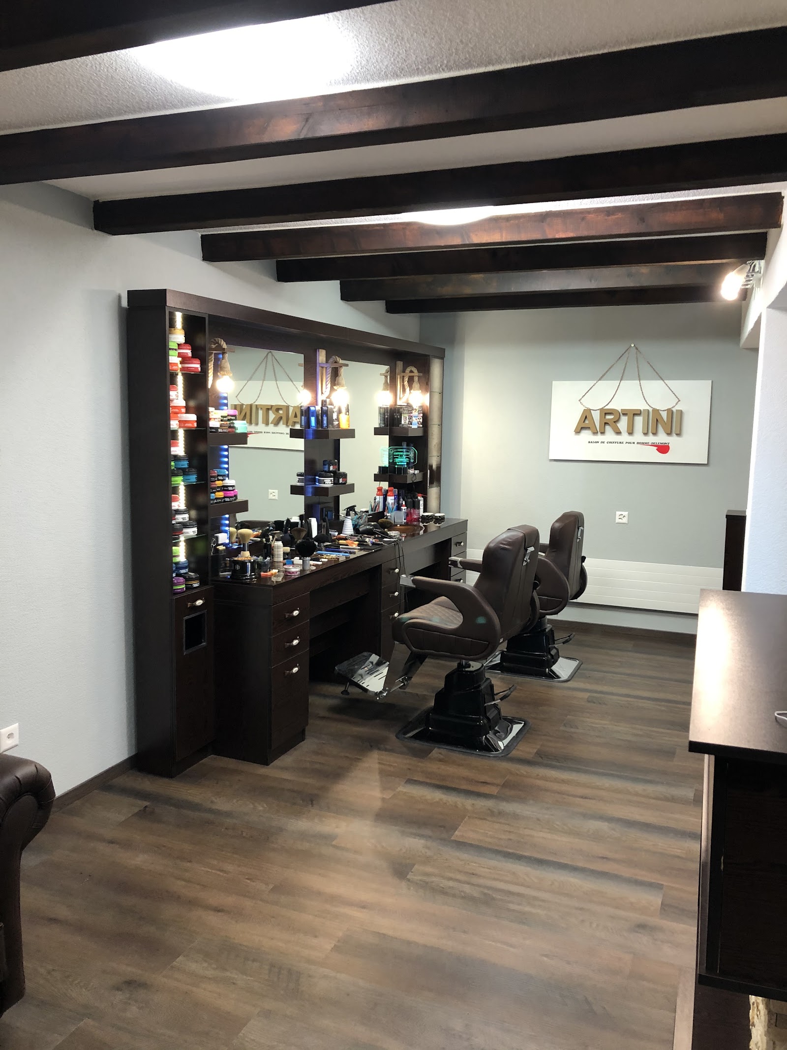 Intérieur du salon Coiffure Artini à Delémont — fauteuils de barbier, miroirs, produits professionnels et enseigne ARTINI